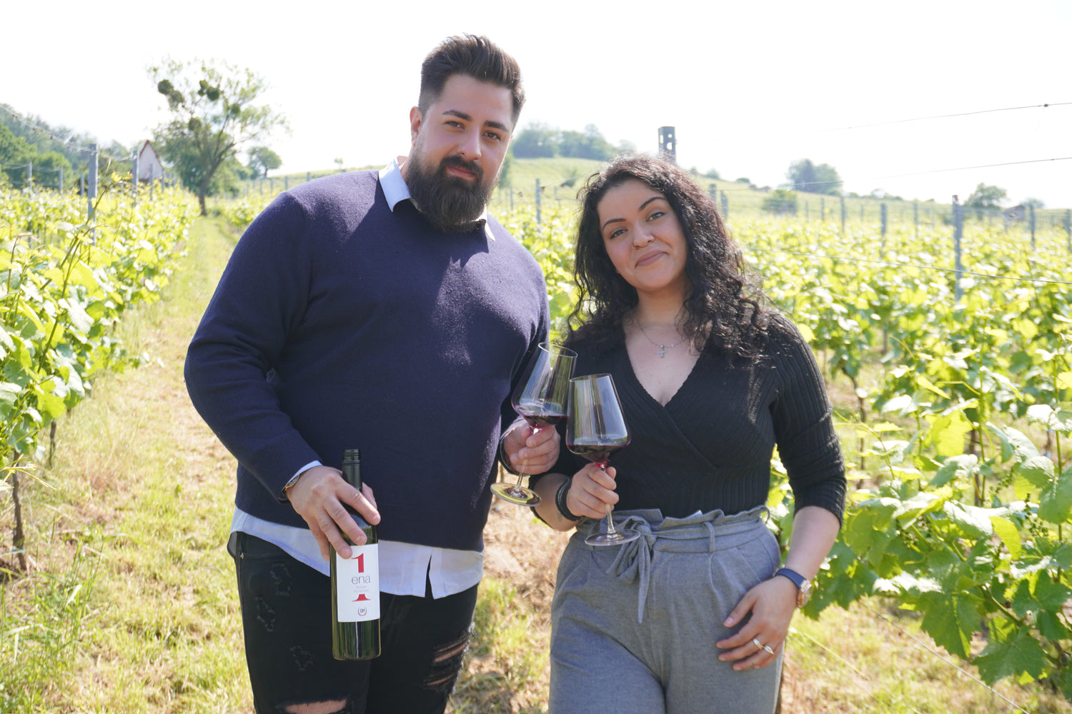 Paar genießt Rotwein im sonnigen Weinberg bei entspannter Stimmung.