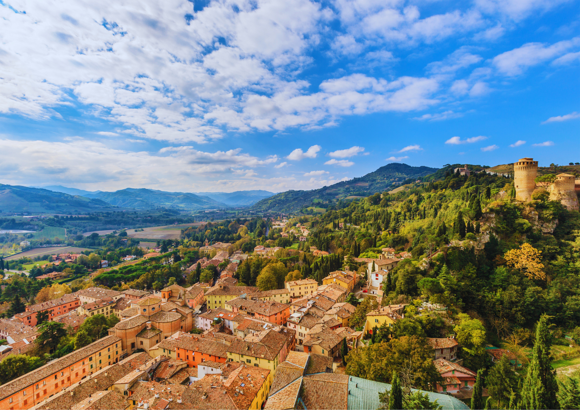Historische Altstadt mit Burg in hügeliger Landschaft unter blauem Himmel.