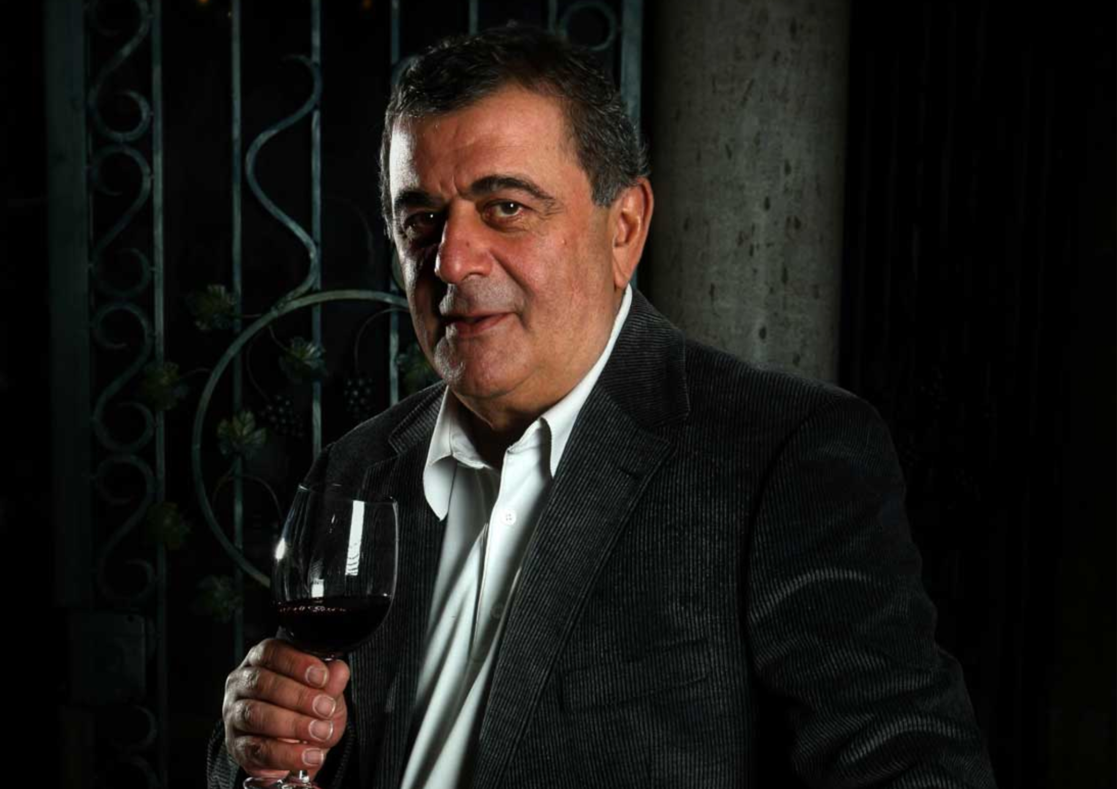 Mann im Anzug hält ein Glas Rotwein vor dunklem, elegantem Hintergrund.