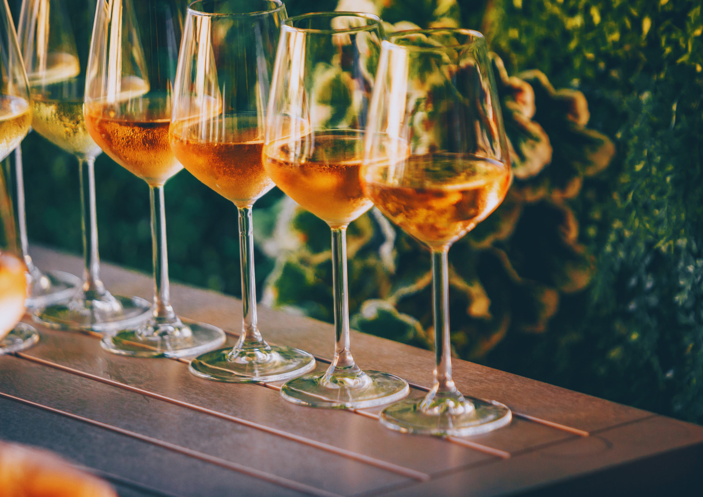 Mehrere Gläser Roséwein auf einem Tisch bei Sonnenuntergang im Grünen.
