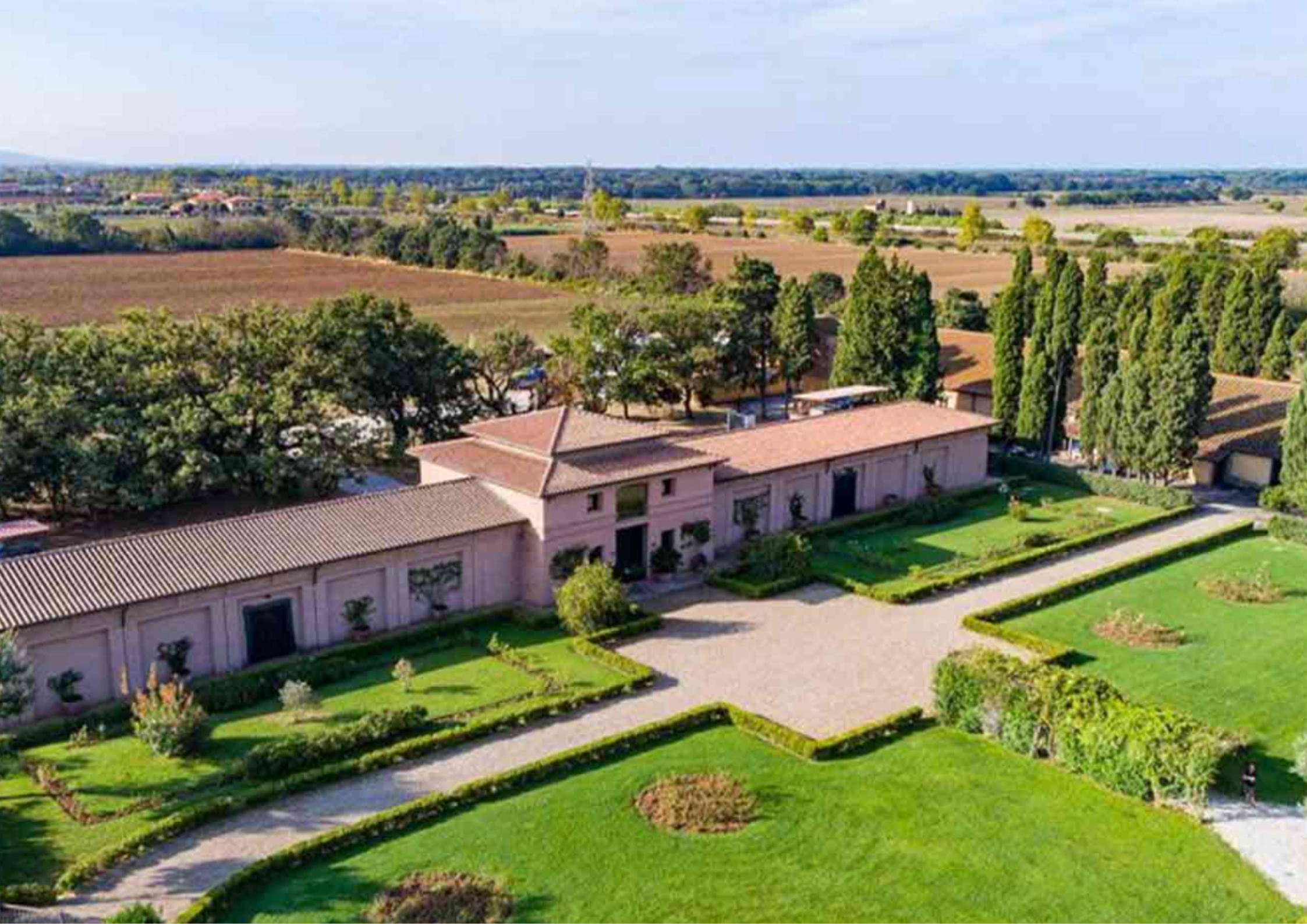 Weingut mit mediterranem Garten in ländlicher Umgebung unter blauem Himmel.