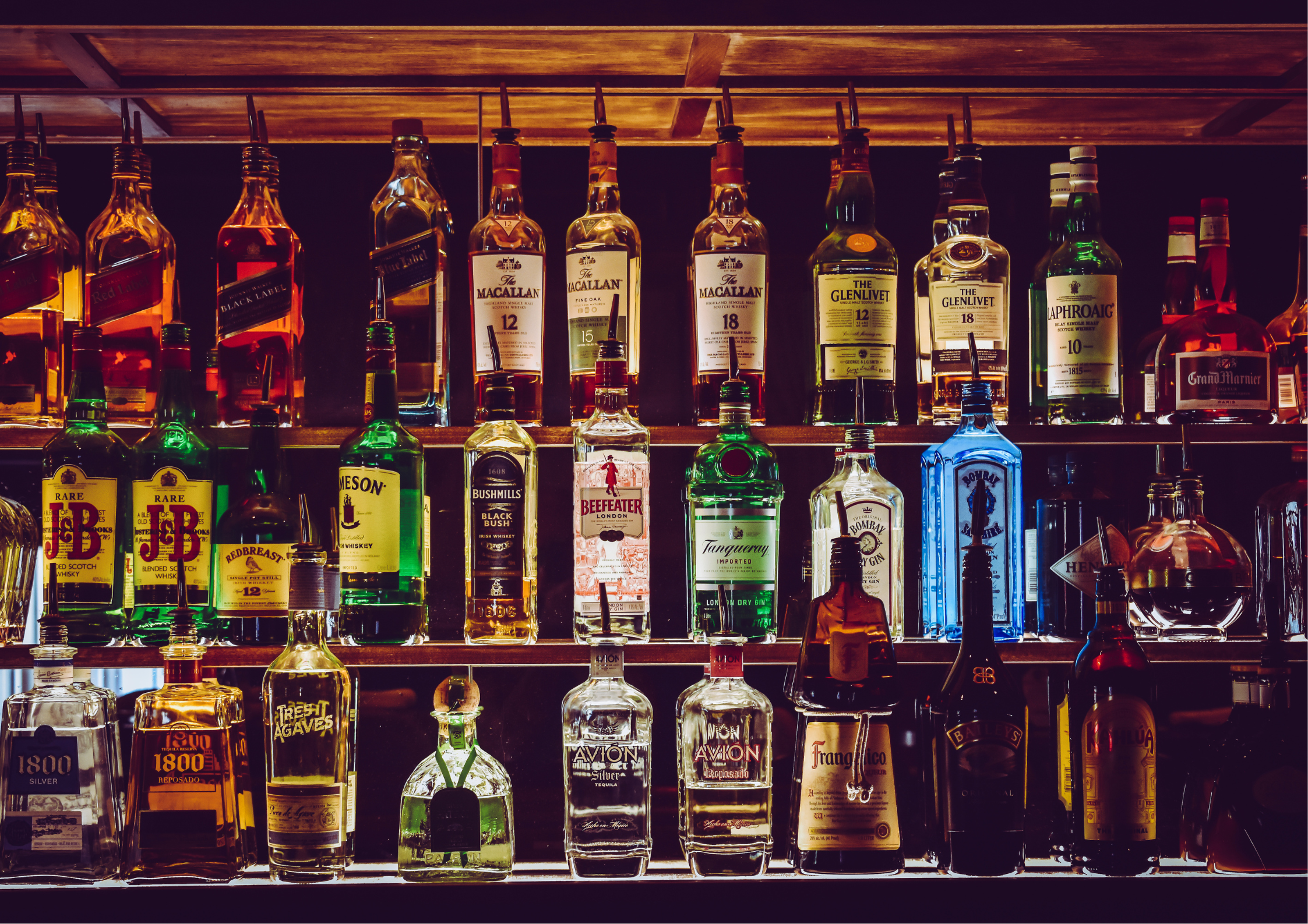 Verschiedene Spirituosenflaschen in einer beleuchteten Bar auf Regalen angeordnet.