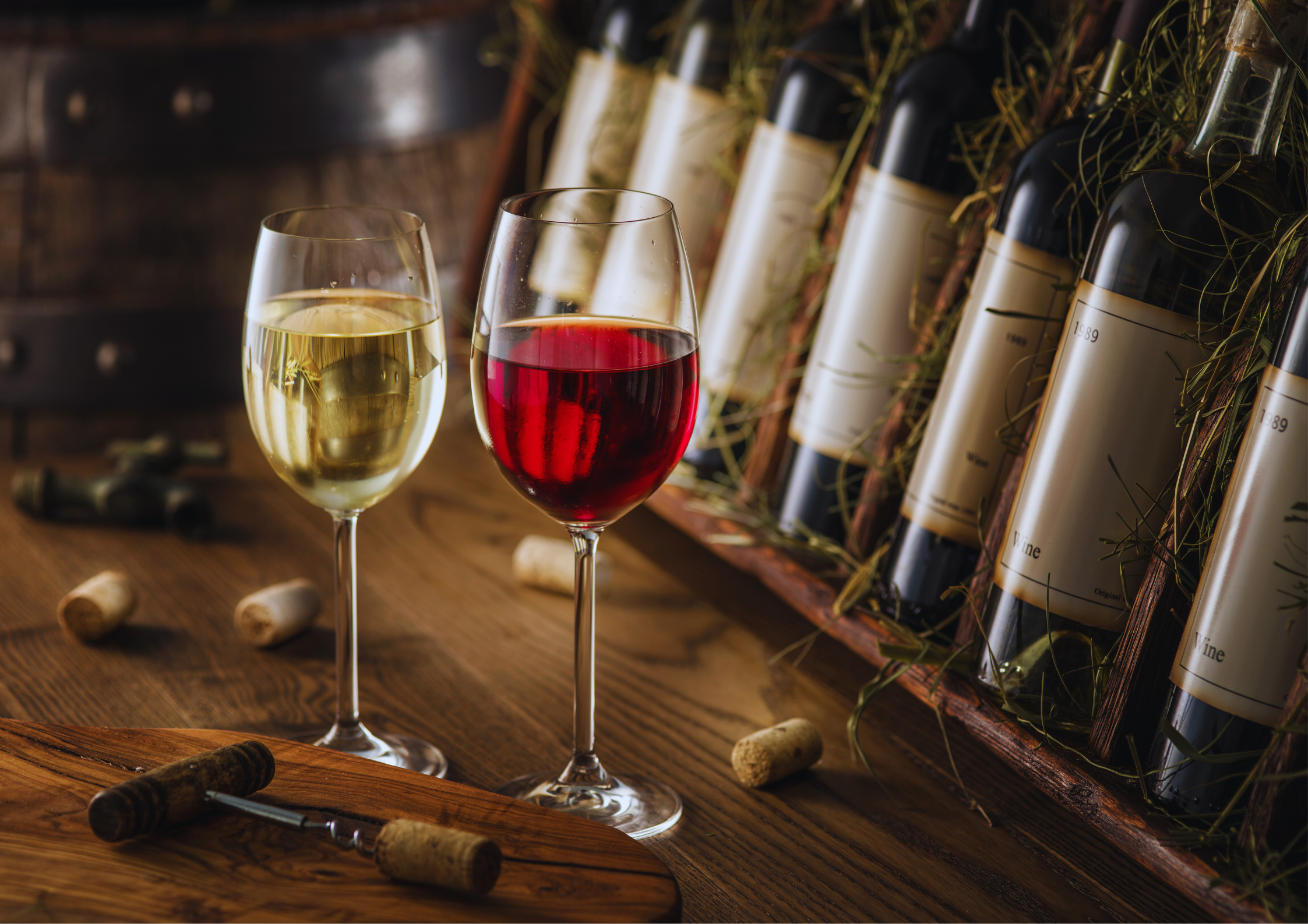 Zwei Gläser Wein, eines weiß und eines rot, vor Weinflaschen und Korken auf Holztisch.