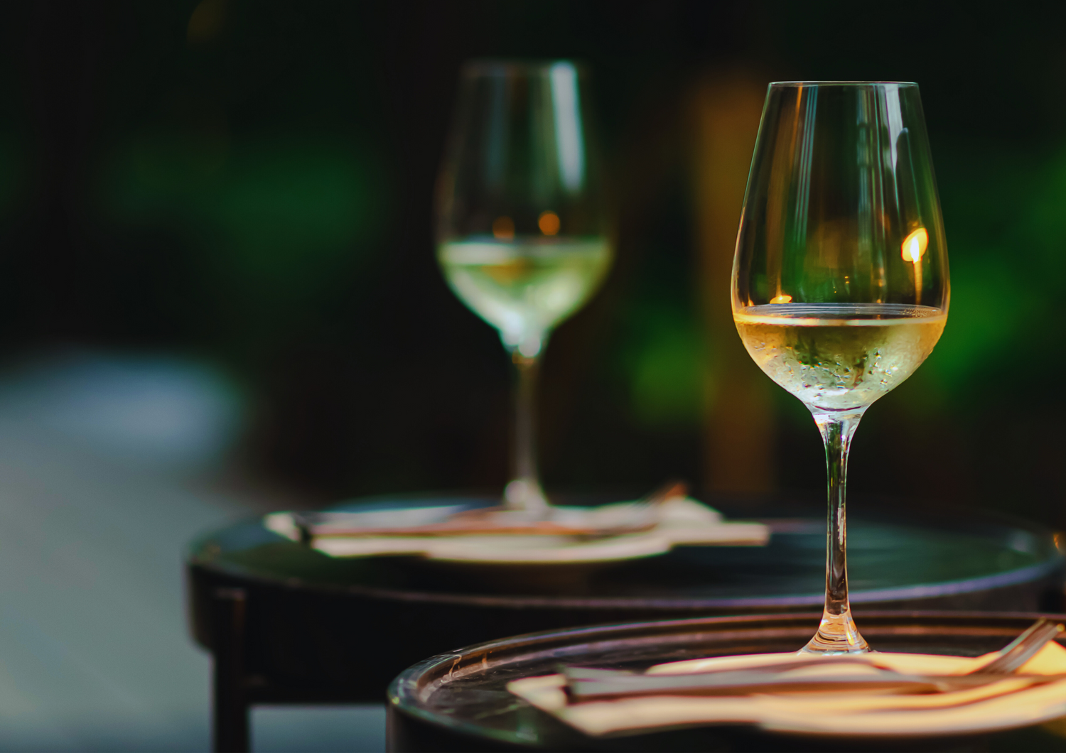 Zwei Gläser Weißwein auf einem Tisch bei Abendstimmung im Freien.