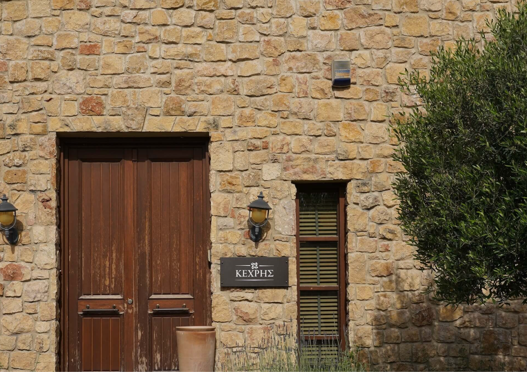 Steinhaus mit Holztür, Fensterläden und Kechris-Schild bei Sonnenschein.