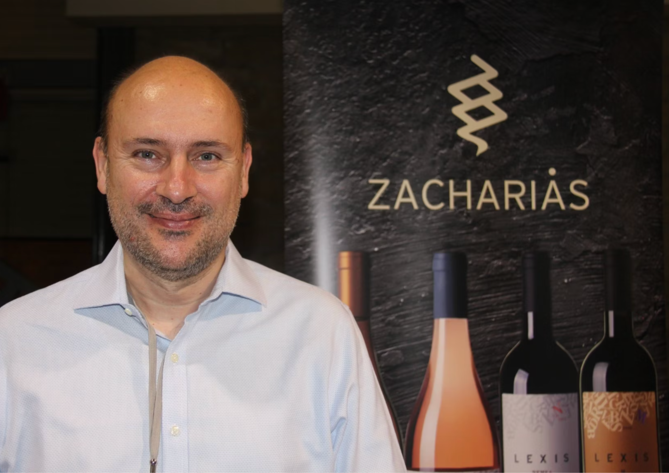 Mann vor Zacharias-Weinplakat mit verschiedenen Flaschen im Hintergrund.