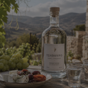 „Flasche griechischer Tsipouro mit Trauben, Feta und Oliven vor einer Berglandschaft“