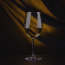„Glas Weißwein vor dunklem Hintergrund mit warmem Lichtspiel“