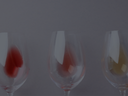 Drei Weingläser mit dezenten Rot- und Weißweinspuren vor ruhigem, grauem Hintergrund.